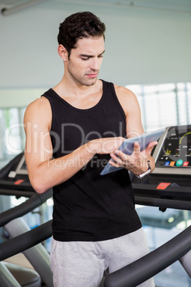 Serious man on treadmill standing with tablet