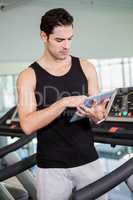 Serious man on treadmill standing with tablet