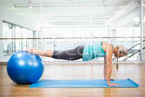 Fit blonde planking on mat with exercise ball