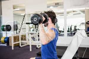 Muscular man lifting dumbbells on bench