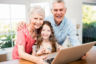 Portrait of smiling grandparents and granddaughter using laptop