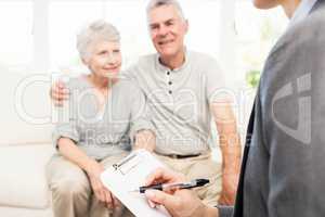 Businesswoman talking with senior couple and writing on clipboar