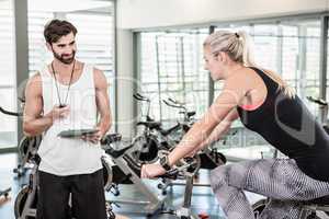 Trainer looking at stopwatch and woman using exercise bike