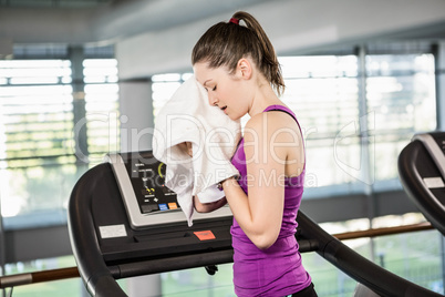 Tired brunette on treadmill wiping sweat with towel