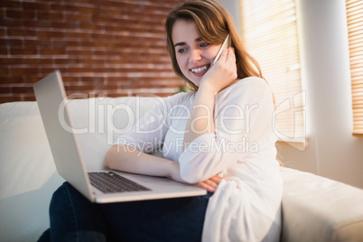 Pretty woman calling on the phone while watching her laptop