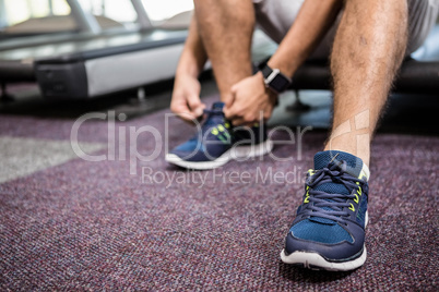 Lower section of man sitting on treadmill and tying the shoelace