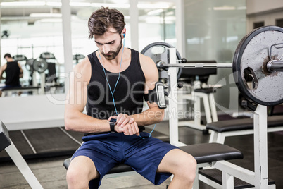 Muscular man sitting on barbell bench and using smartwatch