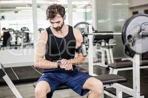 Muscular man sitting on barbell bench and using smartwatch