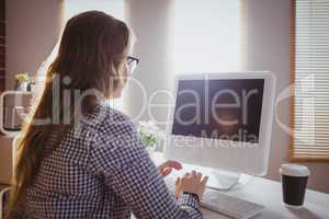 Rear view of hipster businesswoman typing on computer