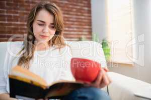 Focused woman reading a book while drinking