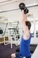 Muscular man lifting dumbbells on bench