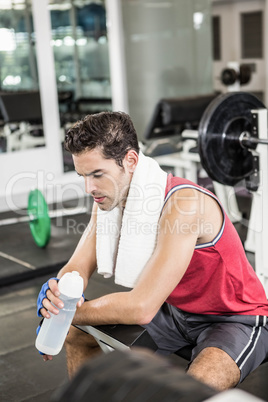 Tired man sitting on bench holding bottle of water