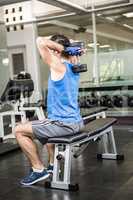 Muscular man lifting dumbbell while sitting on bench