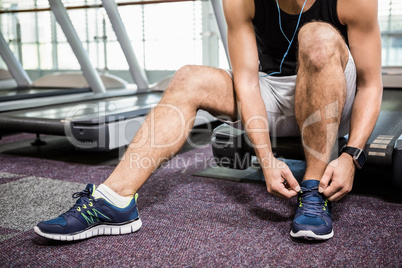 Lower section of man sitting on treadmill and tying the shoelace