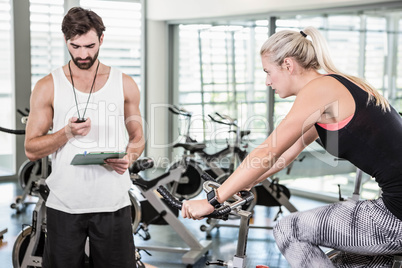 Trainer looking at stopwatch and woman using exercise bike