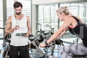 Trainer looking at stopwatch and woman using exercise bike