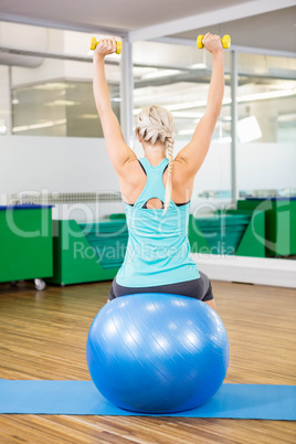 Fit woman lifting dumbbells and sitting on exercise ball