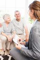 Businesswoman talking with senior couple and writing on clipboar