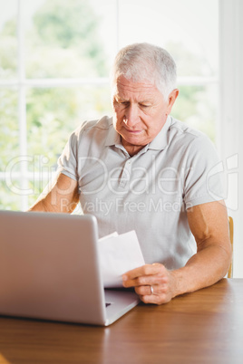 Senior man holding sheets and using laptop