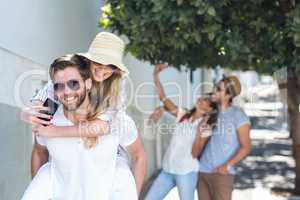 Hip man giving piggy back to his girlfriend and taking selfie