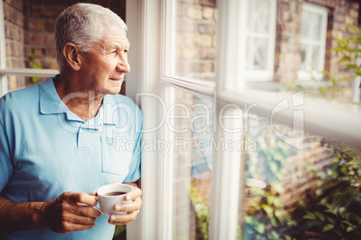 Senior man holding cup and looking out of the window