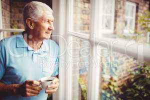 Senior man holding cup and looking out of the window