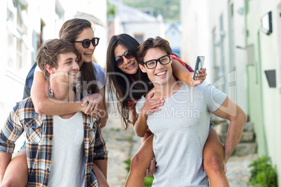 Hip men giving piggy back to their girlfriends and taking selfie