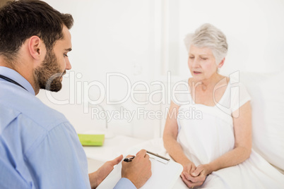 Home nurse listening to elderly woman and writing on clipboard