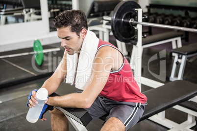 Tired man sitting on bench holding bottle of water