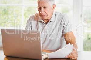 Senior man holding documents and using laptop