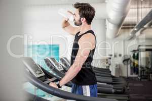 Handsome man drinking water on treadmill