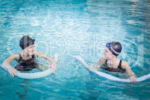 Smiling women in the pool with foam rollers