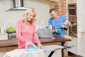 Woman ironing while man having coffee