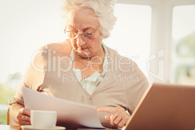 Senior woman dealing with documents while using laptop