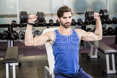 Muscular man lifting dumbbells on bench