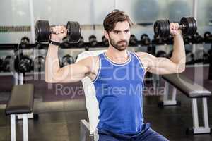 Muscular man lifting dumbbells on bench