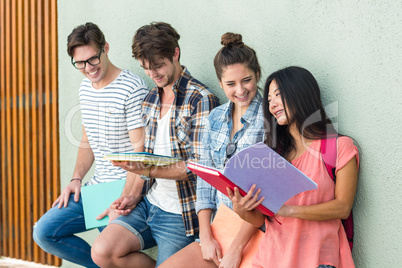 Hip friends leaning against wall and holding notebooks