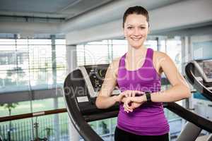 Smiling fit woman using smartwatch on treadmill