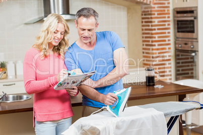 Man ironing while wife reading the news Man ironing while wife reading the news