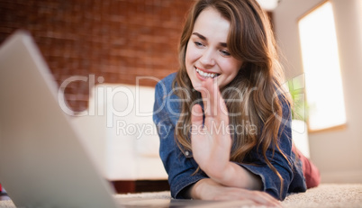 Pretty smiling woman lying on the floor waving at laptop