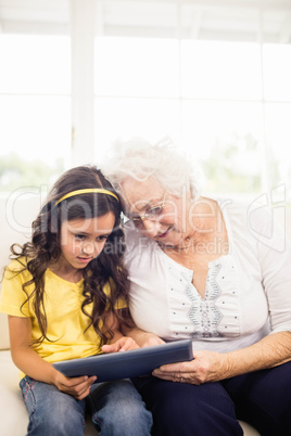 Concentrated granddaughter using tablet with grandmother