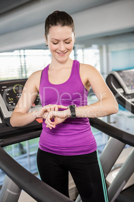 Smiling fit woman using smartwatch on treadmill