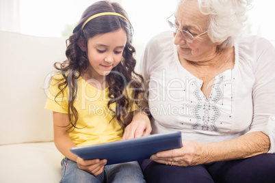 Concentrated granddaughter using tablet with grandmother