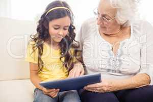 Concentrated granddaughter using tablet with grandmother