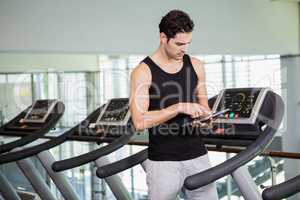 Serious man on treadmill standing with tablet