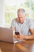 Focused elderly man using smartphone and laptop