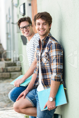 Hip men leaning against wall and holding notebooks