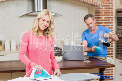 Woman ironing while man having coffee