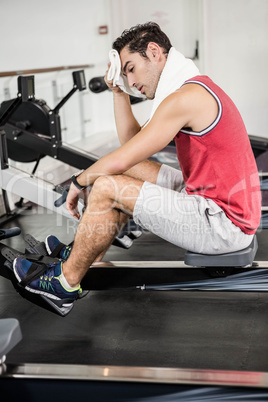 Muscular man on rowing machine wiping sweat with towel