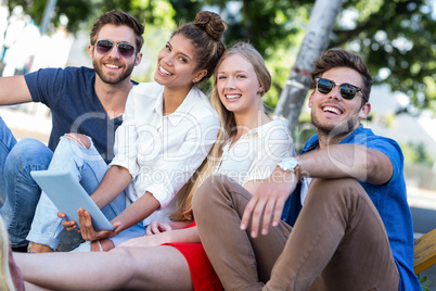 Hip friends holding tablet and sitting on sidewalk